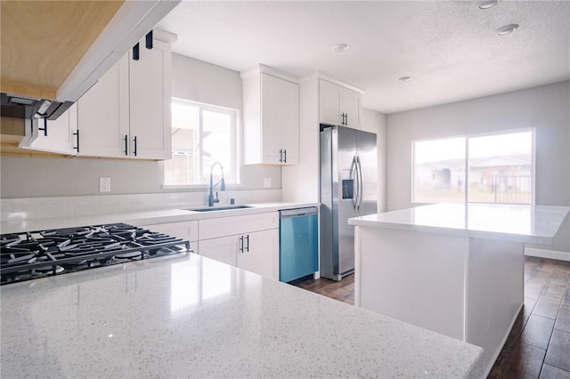 kitchen with dark wood-style floors, appliances with stainless steel finishes, light stone counters, and a sink