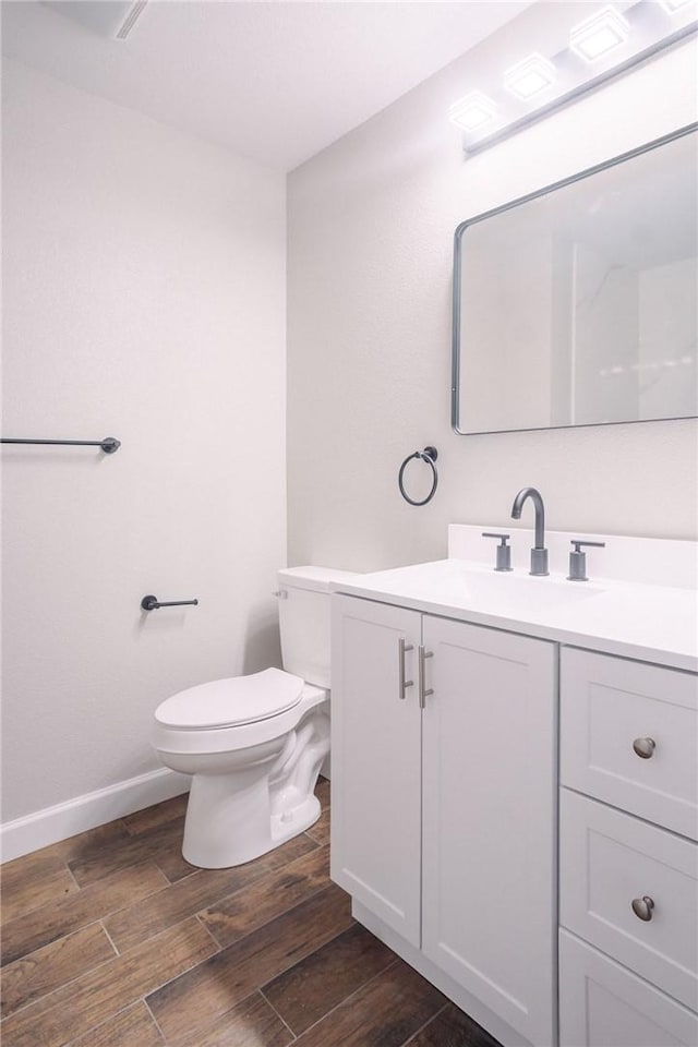 bathroom with vanity, toilet, wood finished floors, and baseboards