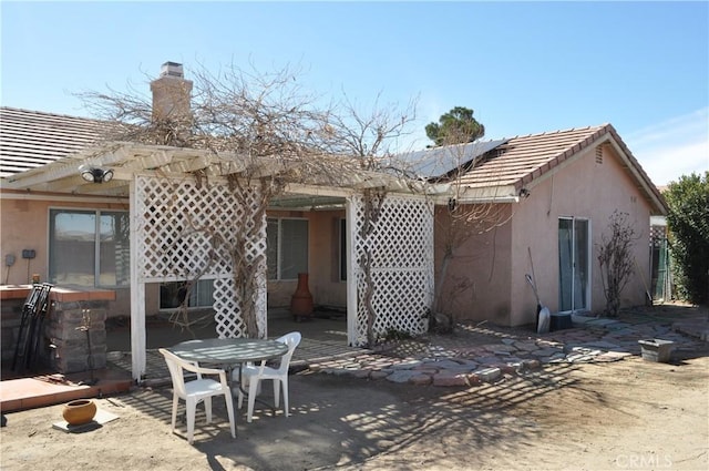 rear view of property with a patio area, stucco siding, a chimney, and a tile roof