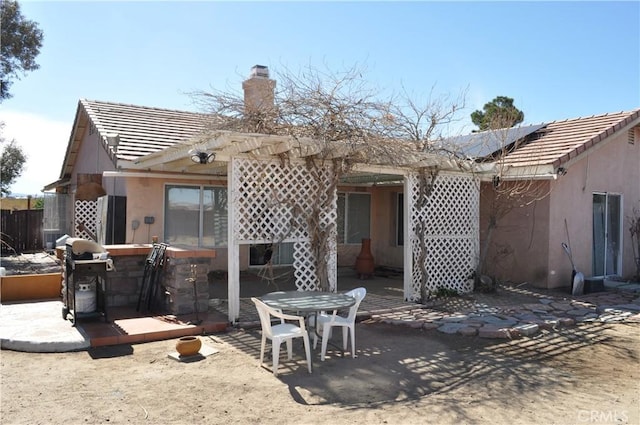 rear view of house with solar panels, a tile roof, stucco siding, a chimney, and a patio area