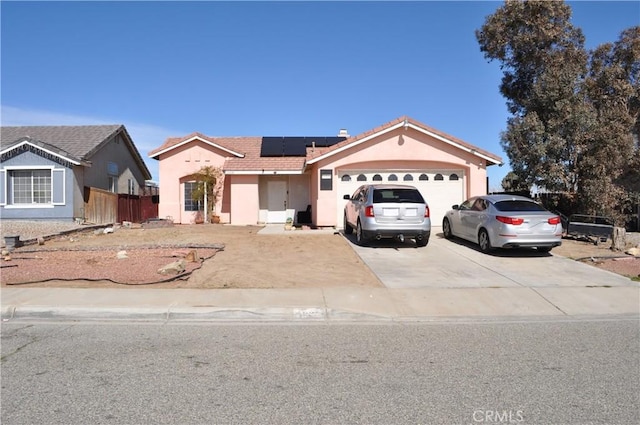 view of front of property featuring solar panels, an attached garage, fence, stucco siding, and driveway