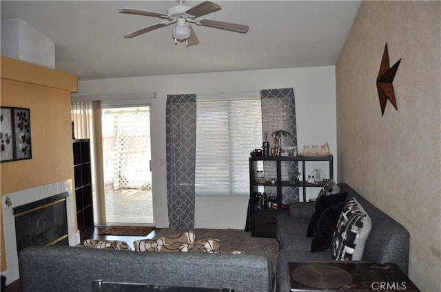 living room with a tile fireplace and ceiling fan