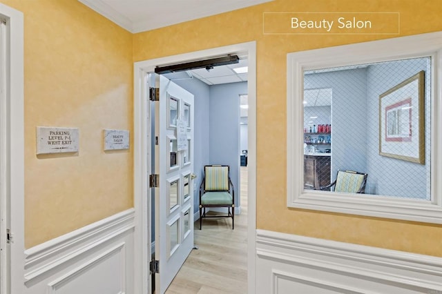 hall with wainscoting, light wood-style floors, and ornamental molding