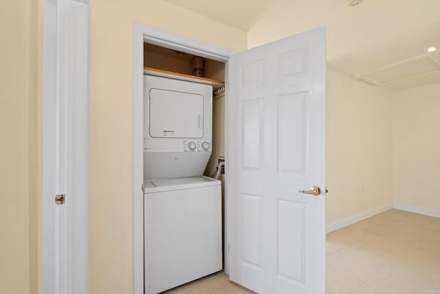 laundry area with baseboards, stacked washer and clothes dryer, light tile patterned flooring, and laundry area