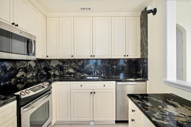 kitchen with a sink, dark stone counters, appliances with stainless steel finishes, and decorative backsplash