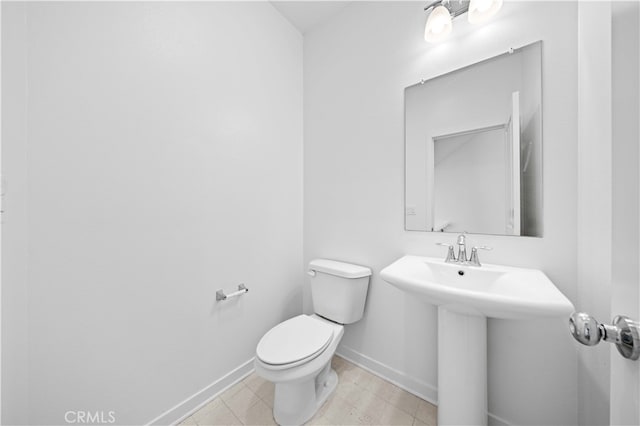half bath featuring tile patterned flooring, toilet, baseboards, and a sink