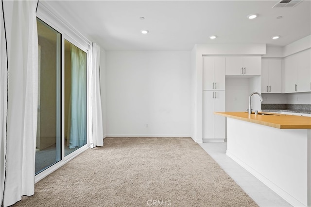 kitchen featuring light colored carpet, butcher block counters, recessed lighting, white cabinetry, and a sink