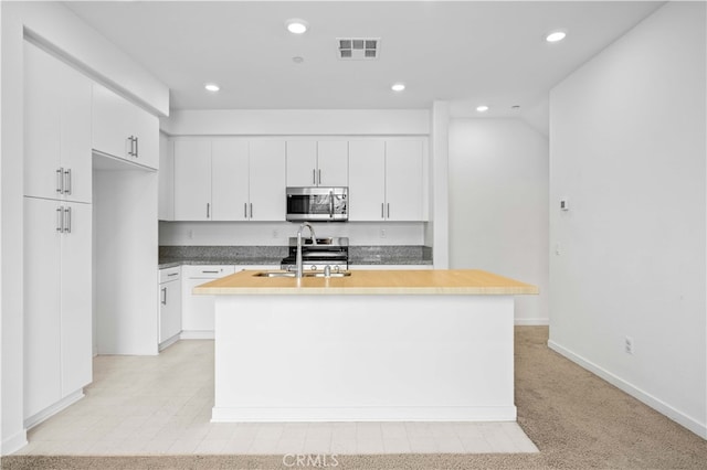 kitchen featuring visible vents, a kitchen island with sink, a sink, stainless steel microwave, and white cabinets