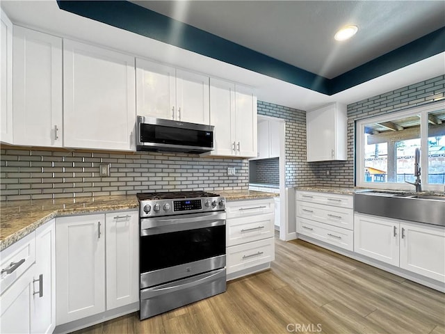 kitchen featuring a sink, backsplash, white cabinetry, appliances with stainless steel finishes, and light wood-style flooring