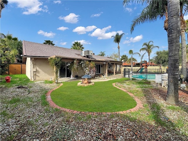 back of property with central AC unit, a tiled roof, an outdoor fire pit, a fenced backyard, and stucco siding