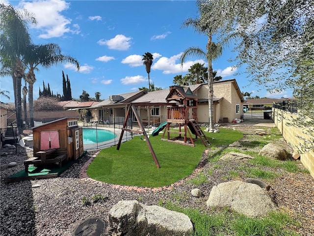 rear view of property with stucco siding, a fenced backyard, a yard, an outdoor pool, and a playground