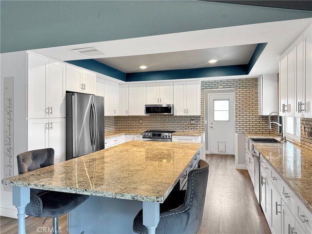 kitchen with a sink, light stone countertops, a kitchen bar, stainless steel appliances, and white cabinets