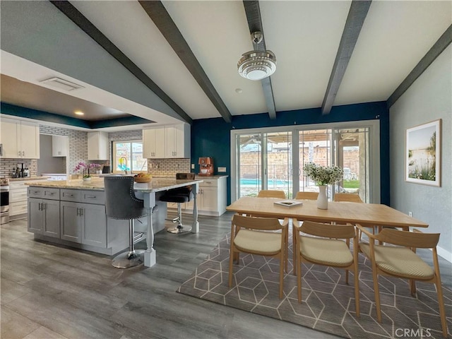 dining space featuring dark wood finished floors, visible vents, beam ceiling, and a raised ceiling