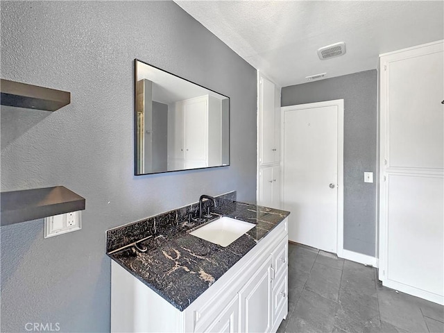 bathroom with a textured wall, visible vents, and vanity
