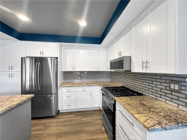 kitchen featuring light stone countertops, wood finished floors, white cabinets, and appliances with stainless steel finishes