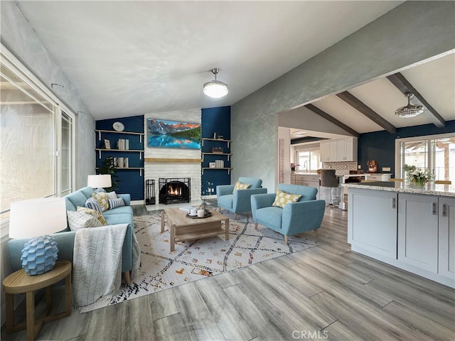living area with lofted ceiling with beams, a lit fireplace, and wood finished floors