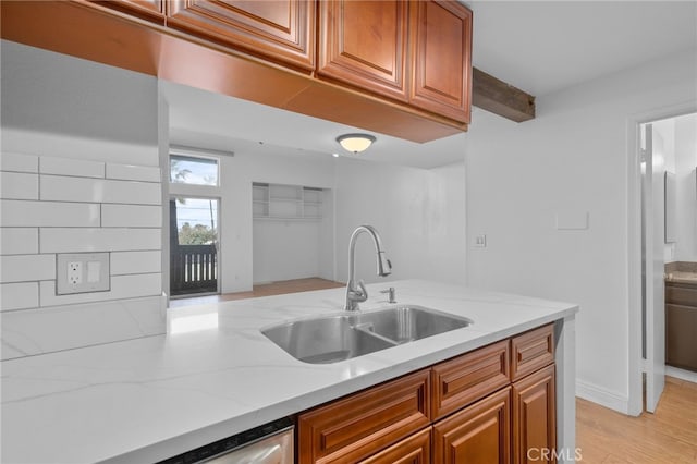 kitchen featuring light wood-type flooring, light stone counters, brown cabinets, and a sink