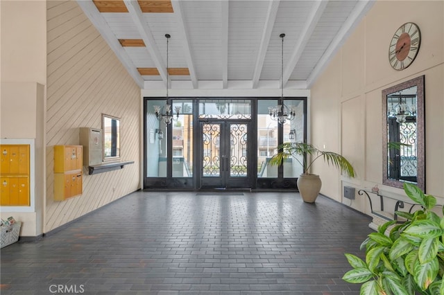 interior space with a chandelier, beam ceiling, french doors, a high ceiling, and brick floor