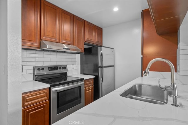 kitchen with light stone countertops, appliances with stainless steel finishes, a sink, tasteful backsplash, and under cabinet range hood