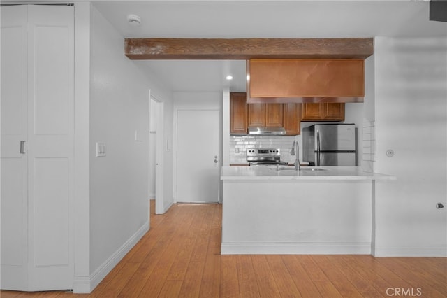 kitchen with under cabinet range hood, tasteful backsplash, stainless steel appliances, light wood-style floors, and brown cabinetry