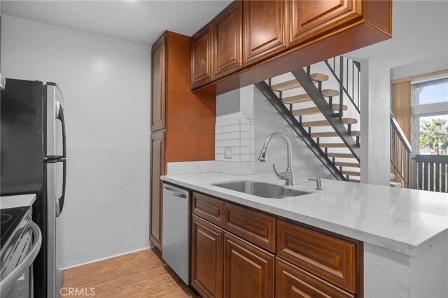 kitchen featuring decorative backsplash, appliances with stainless steel finishes, light wood-type flooring, a sink, and light stone counters
