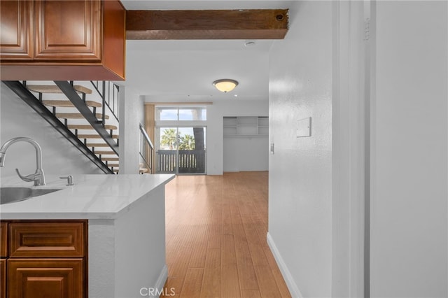 interior space with a sink, baseboards, light wood-type flooring, beamed ceiling, and stairway