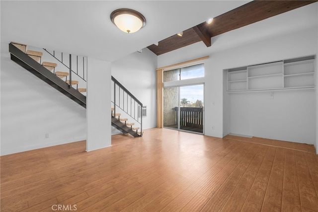 unfurnished living room with high vaulted ceiling, beamed ceiling, stairs, and wood finished floors
