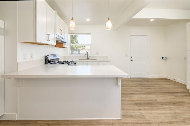 kitchen featuring light wood finished floors, a peninsula, a sink, under cabinet range hood, and gas range