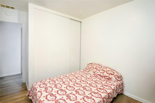 bedroom featuring a closet, visible vents, baseboards, and wood finished floors