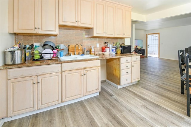 kitchen featuring light wood finished floors, baseboards, backsplash, and a sink