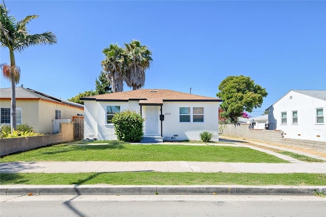 view of front facade featuring stucco siding, a front yard, and fence