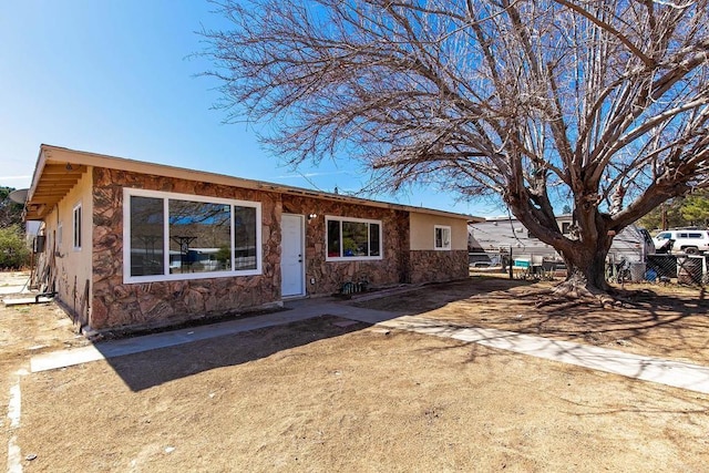 ranch-style house featuring stone siding, stucco siding, and fence