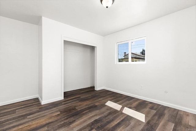 unfurnished bedroom with a closet, baseboards, and dark wood-style flooring