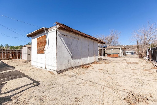 view of property exterior with an outbuilding, a jacuzzi, a storage unit, and fence