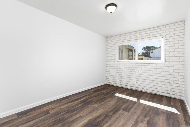 unfurnished room featuring baseboards, brick wall, and dark wood-style flooring