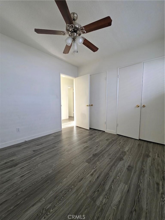 unfurnished bedroom featuring baseboards, two closets, a ceiling fan, and dark wood-style flooring