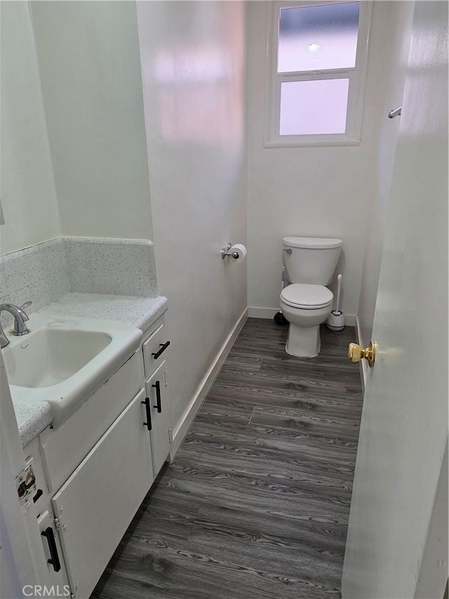 bathroom featuring baseboards, toilet, wood finished floors, and vanity