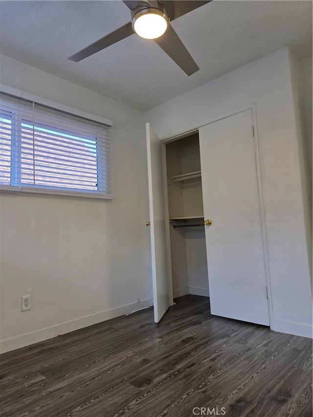 unfurnished bedroom with dark wood finished floors, baseboards, a closet, and ceiling fan