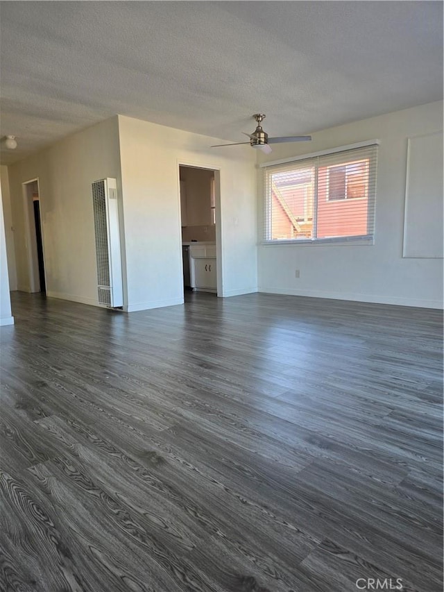 empty room with dark wood-style floors, a ceiling fan, baseboards, and a textured ceiling