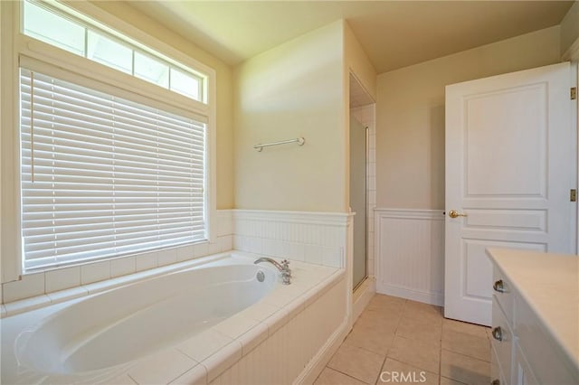 full bath with tile patterned flooring, wainscoting, a garden tub, and a healthy amount of sunlight