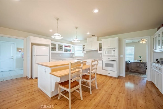 kitchen featuring light wood finished floors, glass insert cabinets, decorative backsplash, white cabinets, and white appliances