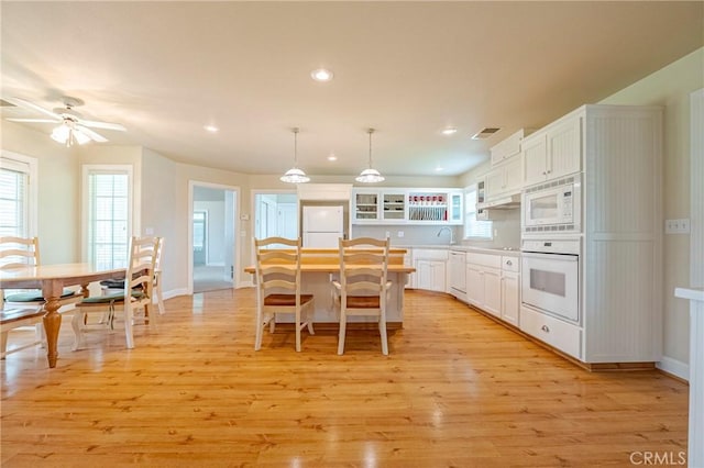 kitchen with white appliances, visible vents, a kitchen island, light wood-style flooring, and white cabinets