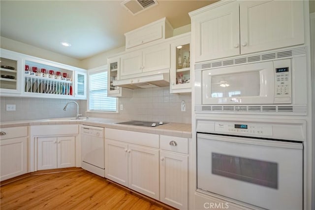 kitchen with white appliances, visible vents, a sink, tile counters, and under cabinet range hood