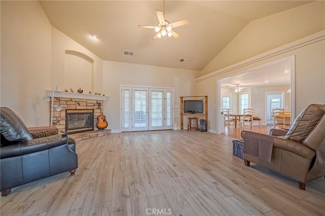 living room featuring light wood finished floors, a stone fireplace, visible vents, and a ceiling fan