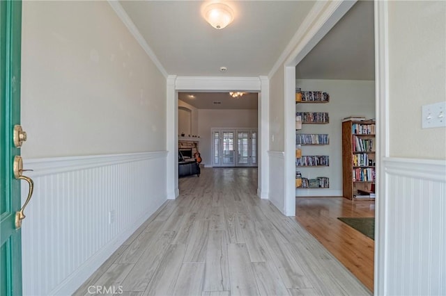 foyer featuring a fireplace, ornamental molding, wainscoting, and light wood finished floors