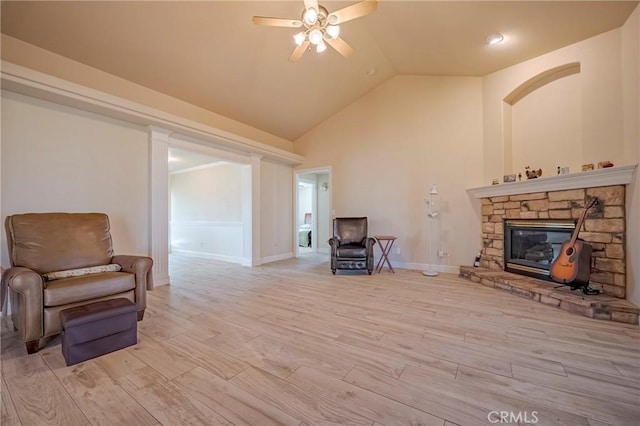 living area with high vaulted ceiling, light wood-style flooring, a ceiling fan, a fireplace, and baseboards