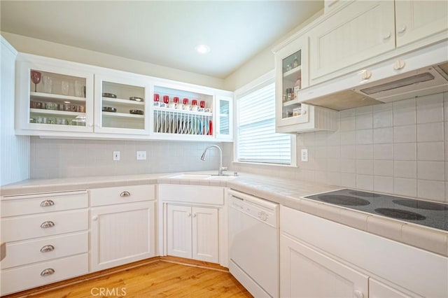 kitchen with white dishwasher, a sink, tile counters, under cabinet range hood, and black electric cooktop