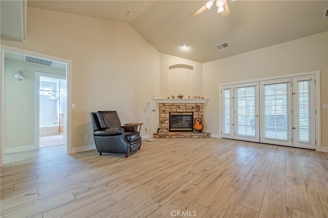 living area featuring a stone fireplace, a ceiling fan, visible vents, and light wood finished floors