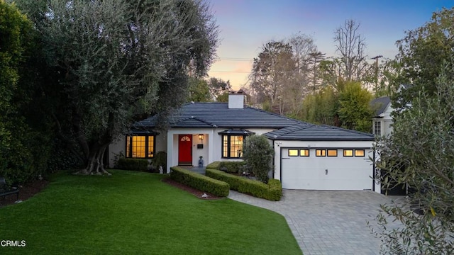 view of front of property featuring a front lawn, a tile roof, a chimney, decorative driveway, and an attached garage