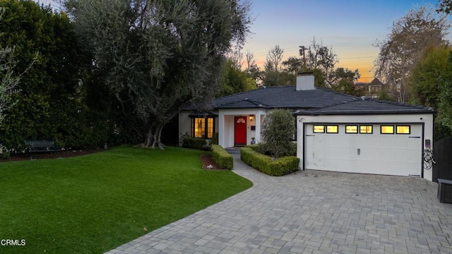 view of front of property with a tiled roof, a lawn, a chimney, and stucco siding